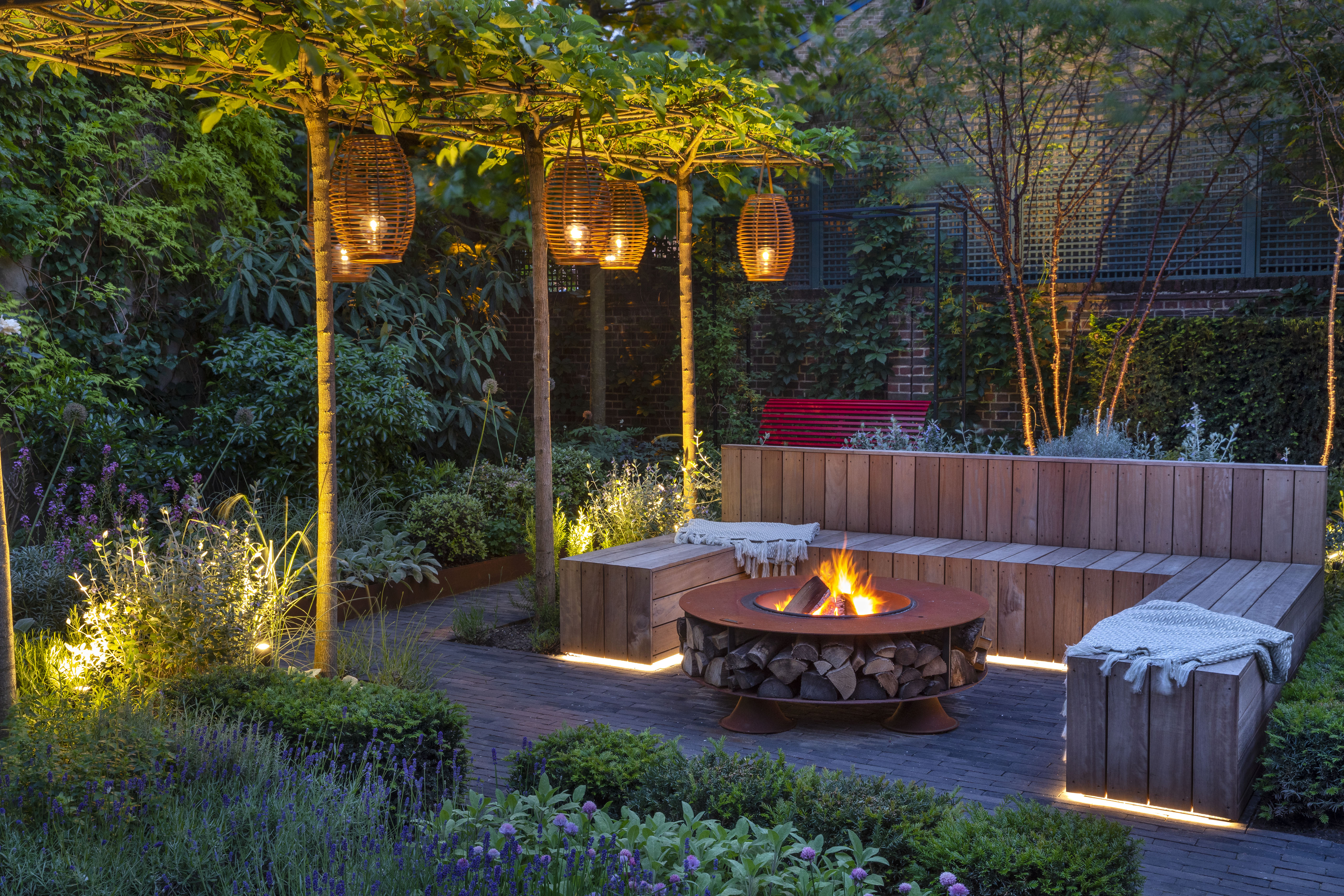 “A backyard firepit burning brightly at dusk, with string lights overhead
