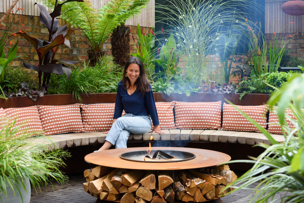 Deisgner sat on bespoke curved bench next to fire pit which is key feature of garden